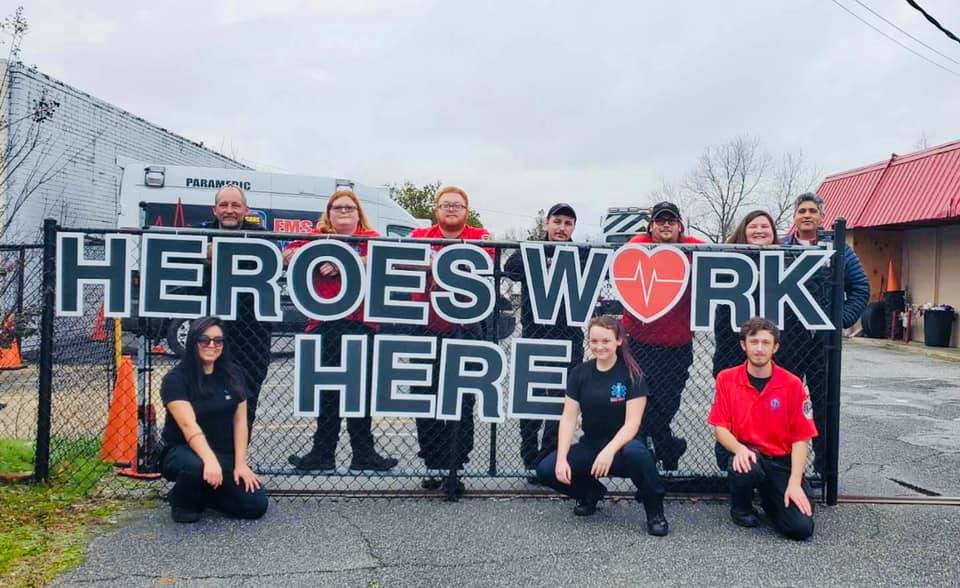 Amulance team standing in front of sign that says 'heroes work here'